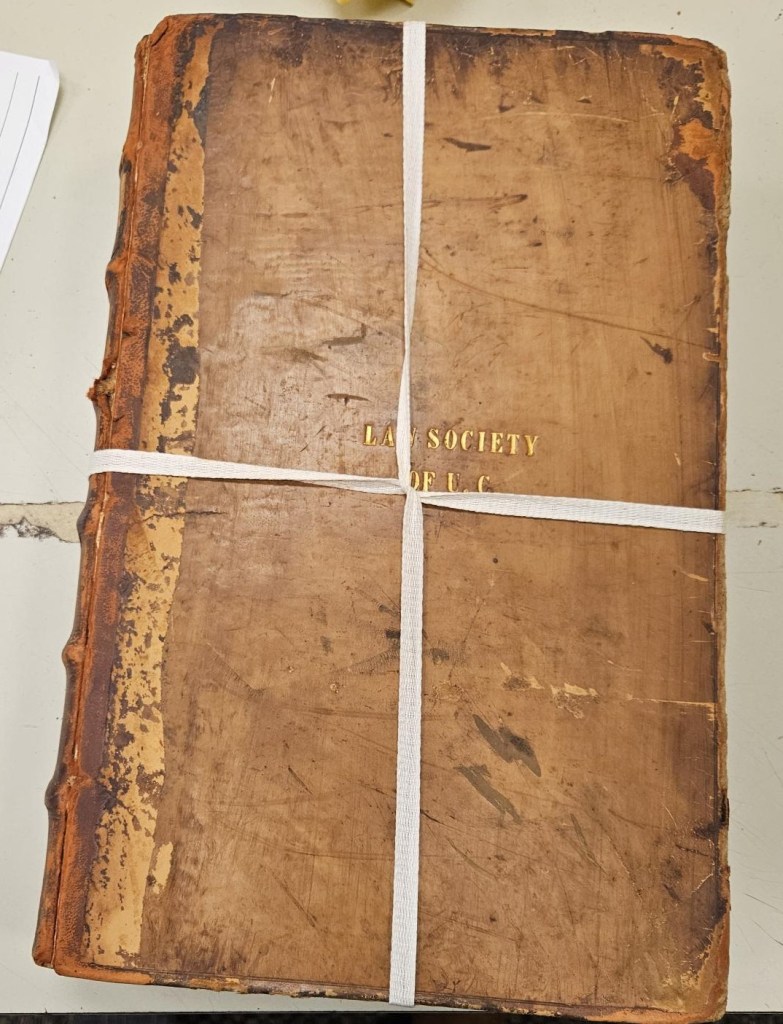 A photograph of an old worn book, held together with white cotton twill tape tied in a plus pattern.